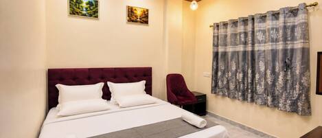 A bedroom with a large bed, a chair, a nightstand, and two paintings on the wall.