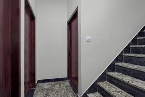 Un pasillo con piso alfombrado, una escalera de peldaños oscuros y puertas de madera.