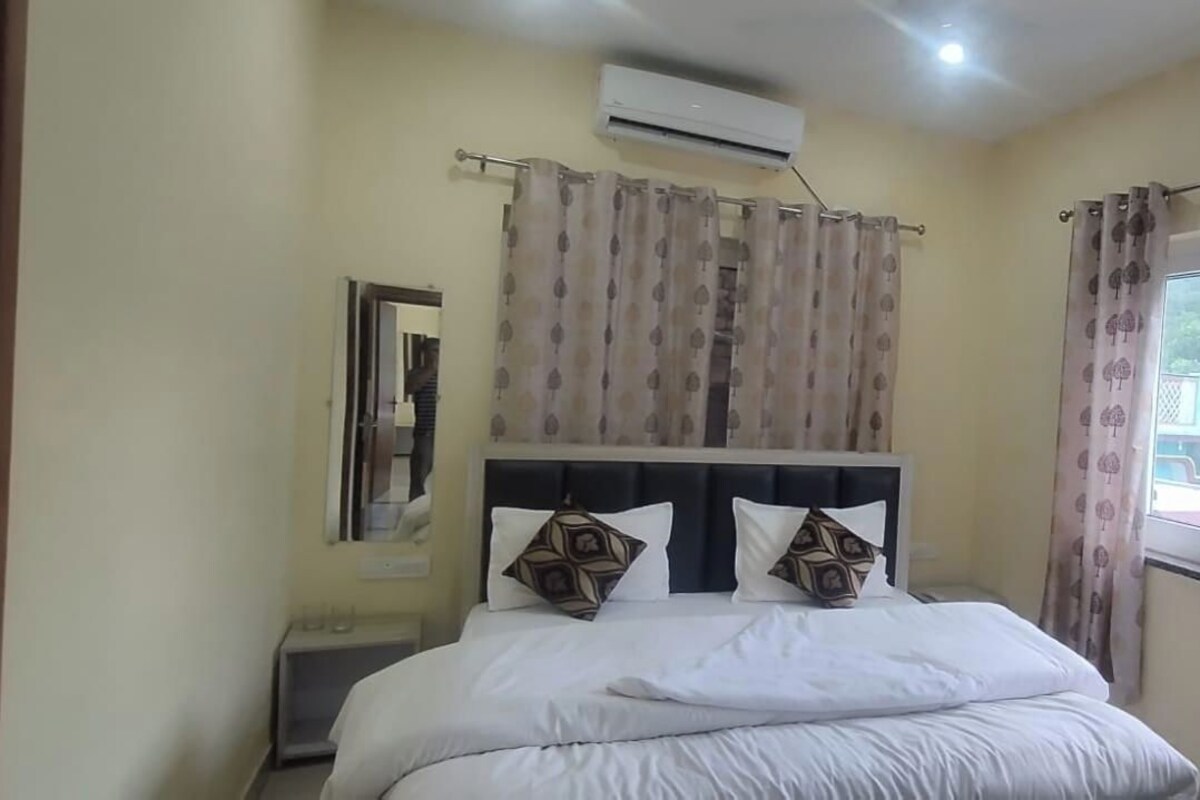 A hotel room with a bed, a nightstand, a mirror, and a window with curtains.
