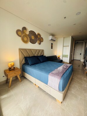 A modern bedroom with a large bed, bedside tables, a wall-mounted air conditioner, and a decorative wall piece. - Bello Horizonte Oceanfront Apartment Suite (Santa Marta)