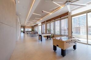 A spacious indoor area with a foosball table, a ping pong table, and large windows allowing natural light. - Bello Horizonte Oceanfront Apartment Suite (Santa Marta)