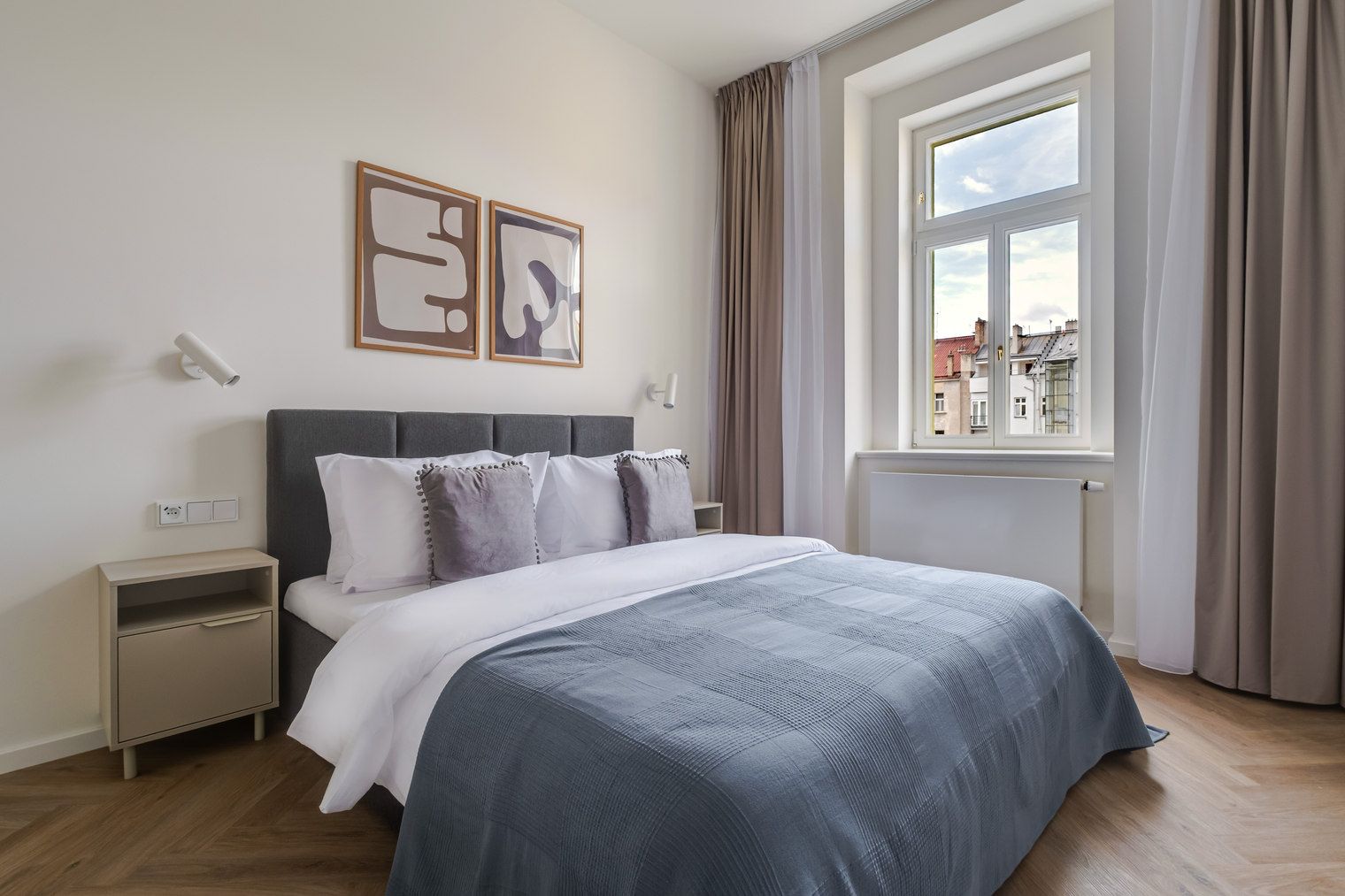 A bedroom with a bed, bedside tables, a window with curtains, and artwork on the wall.