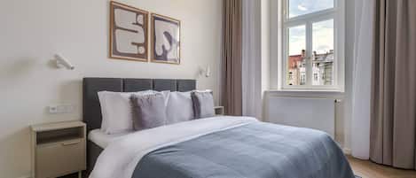 A bedroom with a bed, bedside tables, a window with curtains, and artwork on the wall.