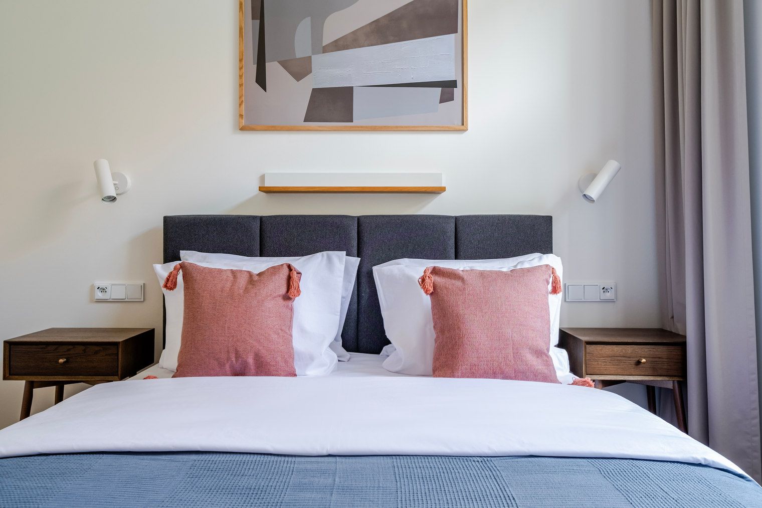 A hotel room with a bed, two nightstands, a wall-mounted light, and a painting above the bed.