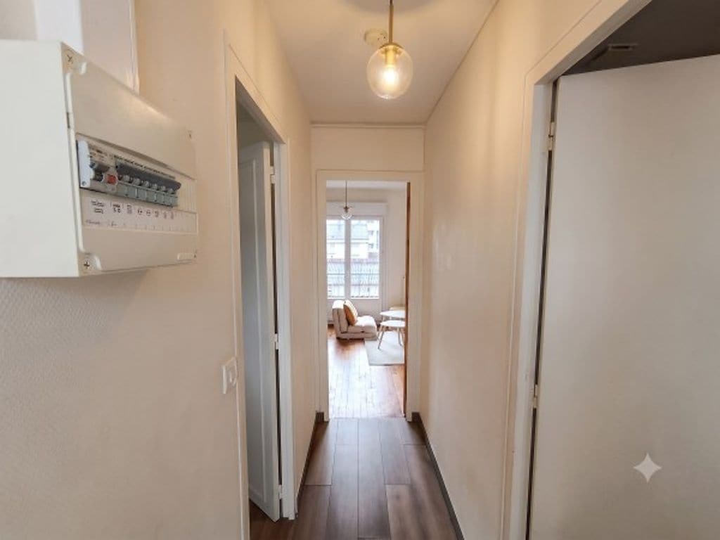 Corredor com luminária, porta e vista para um quarto com sofá e janela.