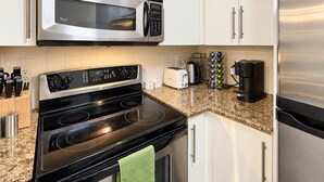 A kitchen with stainless steel appliances, including a microwave and a stove, with a granite countertop and white cabinetry.