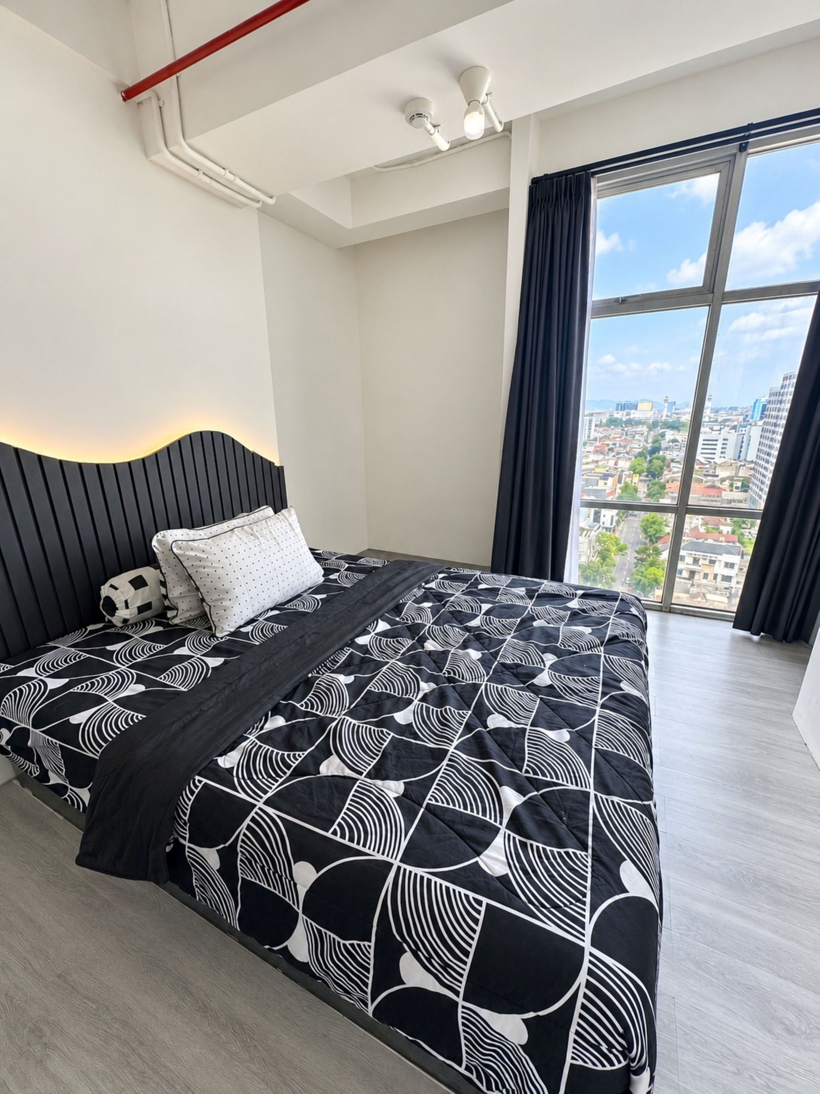 Un dormitorio moderno con una cama grande, un cabecero y vistas de la ciudad a través de un ventanal.