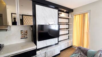 A modern living room with a flat-screen TV mounted on a marble wall, a sofa, and a dining area with a table.