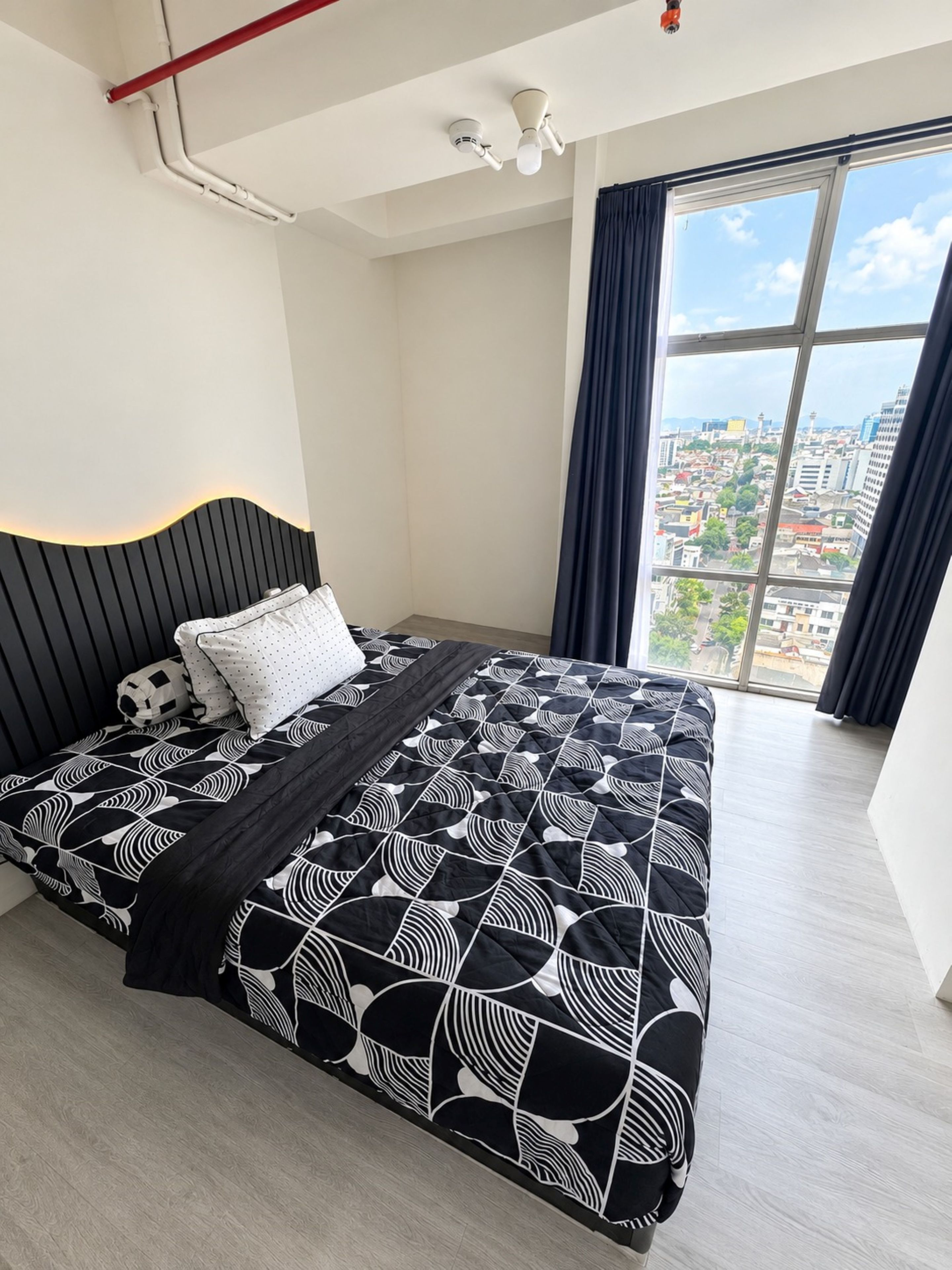 A modern bedroom with a large bed, a city view, and a ceiling fan.