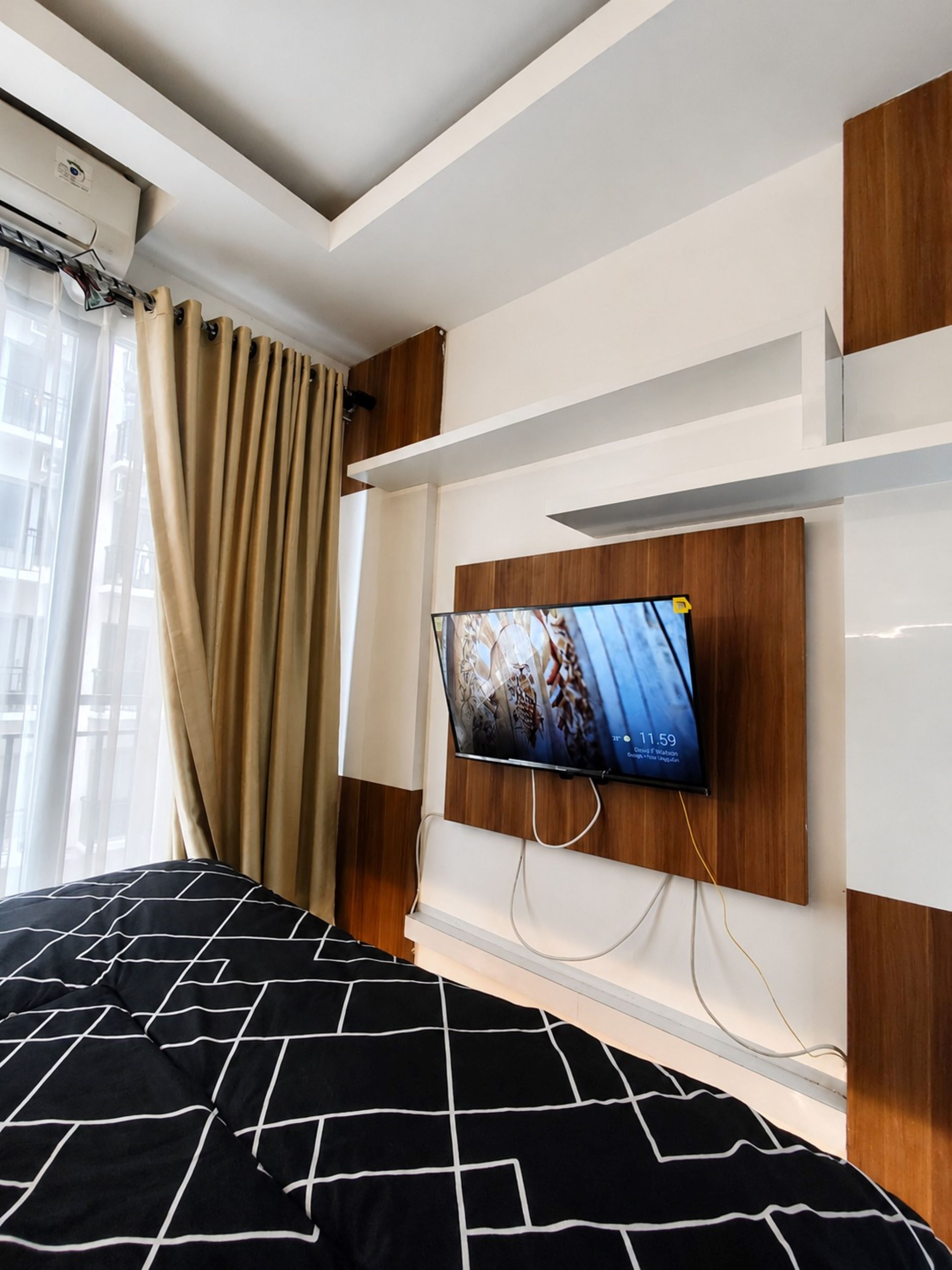 A hotel room with a bed, a mounted television, and a window with curtains.