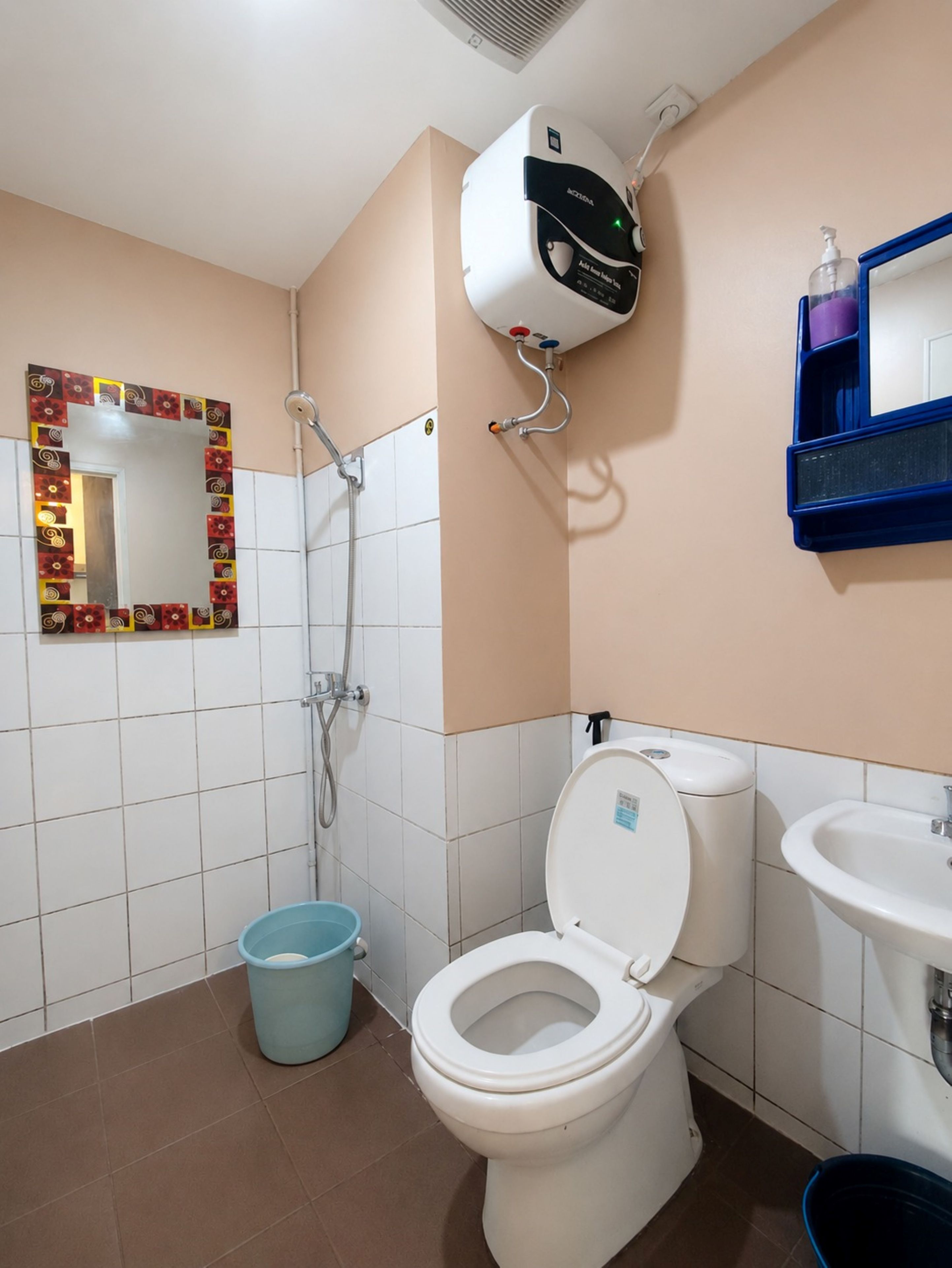 A bathroom with a toilet, a sink, a shower, and a mirror with a decorative frame.