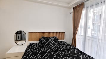 A bedroom with a bed, a bedside table, a mirror, and a window with curtains.