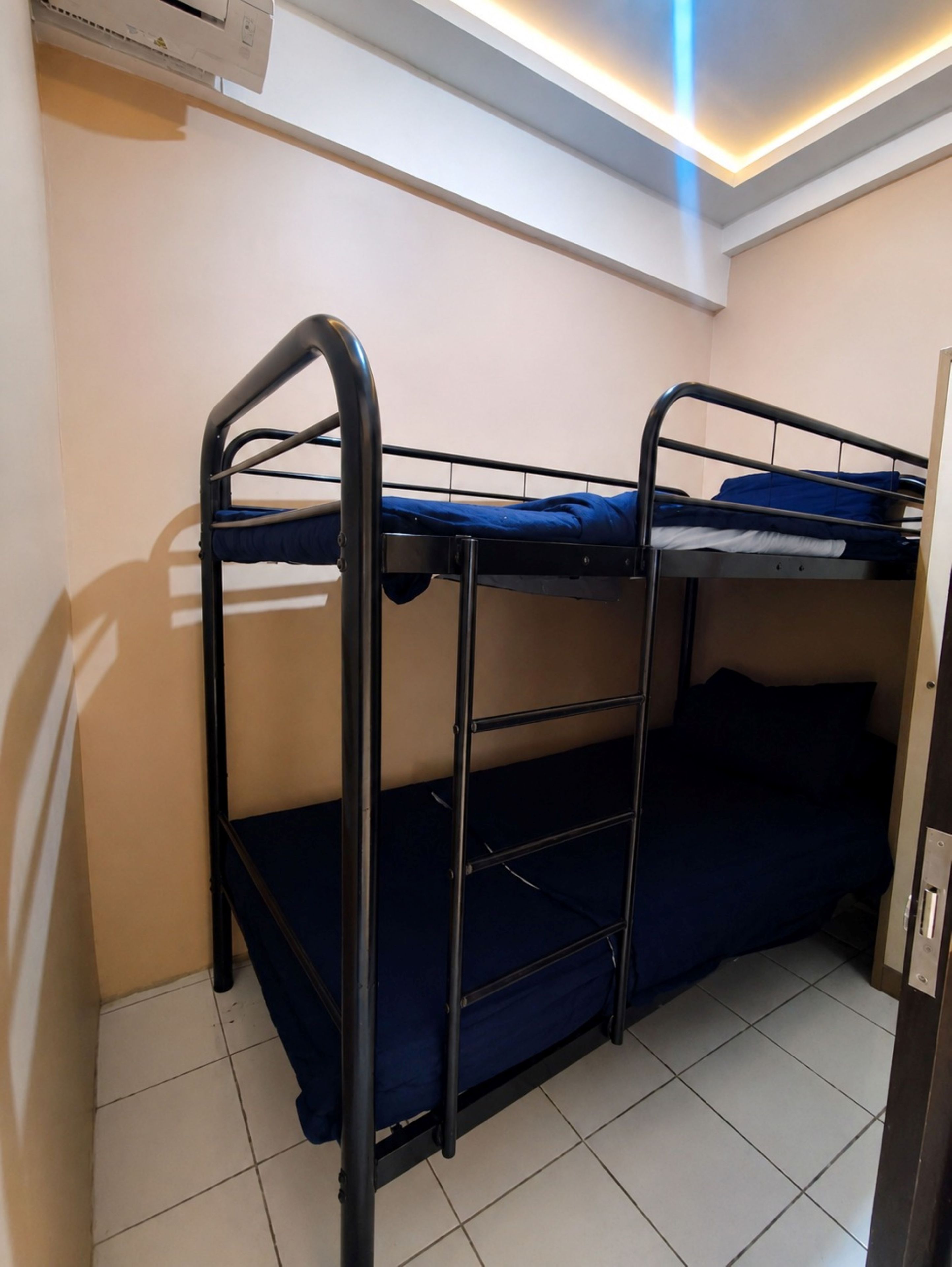 A bunk bed with a metal frame and blue bedding, a tiled floor, and a ceiling with recessed lighting.