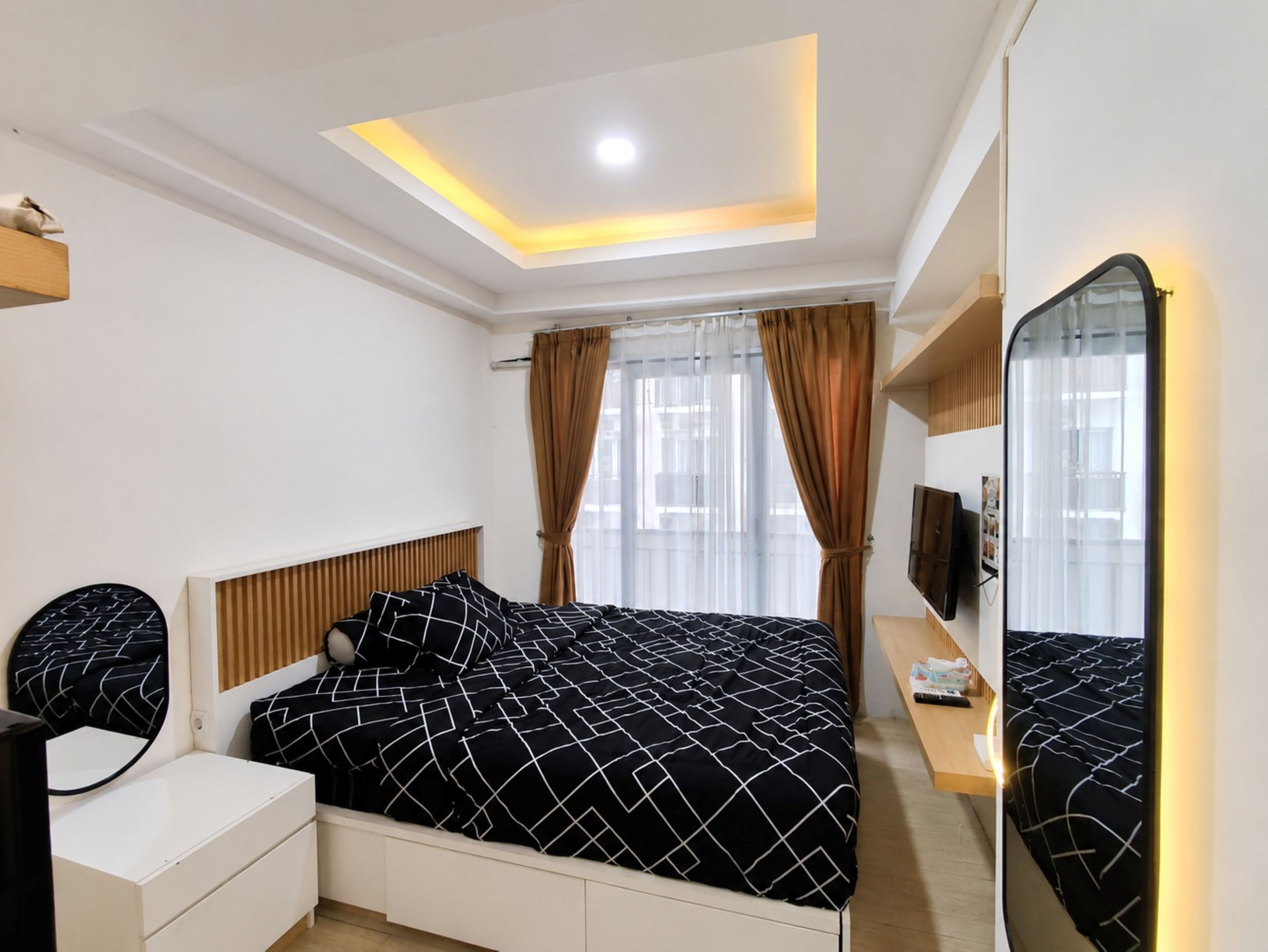 A bedroom with a bed, a bedside table, a mirror, and a ceiling light.