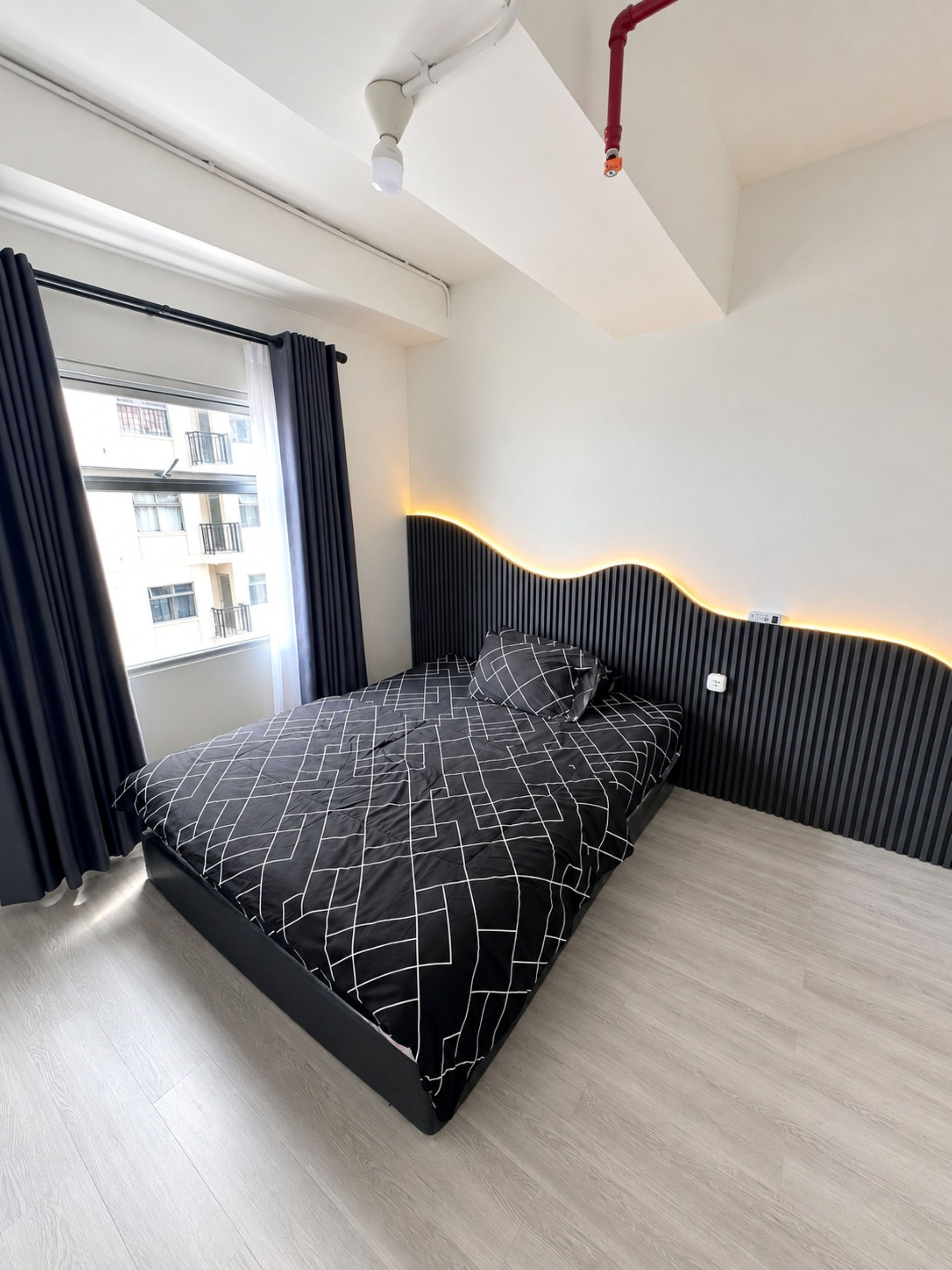 A modern bedroom with a bed, a window with curtains, and a view of buildings outside.