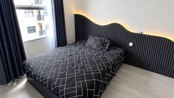 A modern bedroom with a bed, a window with curtains, and a view of buildings outside.