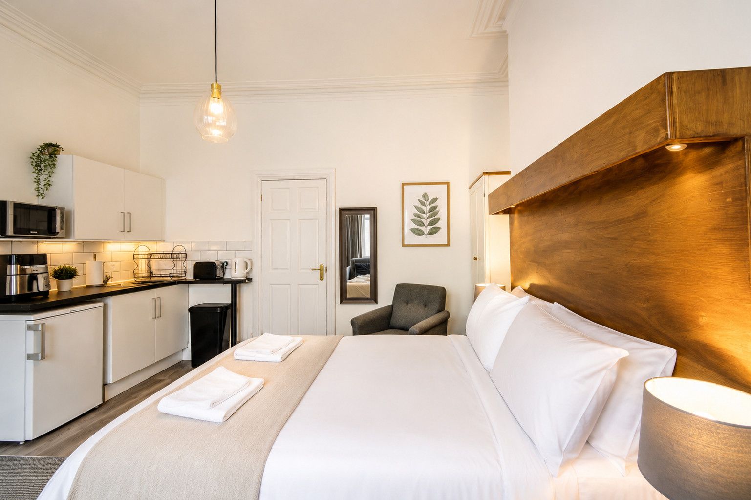 A hotel room with a bed, a chair, a desk with a microwave, and a kitchenette.