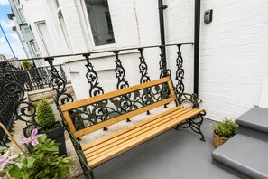 A wooden bench with ornate black metal railings, positioned on a balcony with a white wall and a small potted plant. - K Suites - Wellesley Road 1 (One bedroom Studio) (Great Yarmouth)