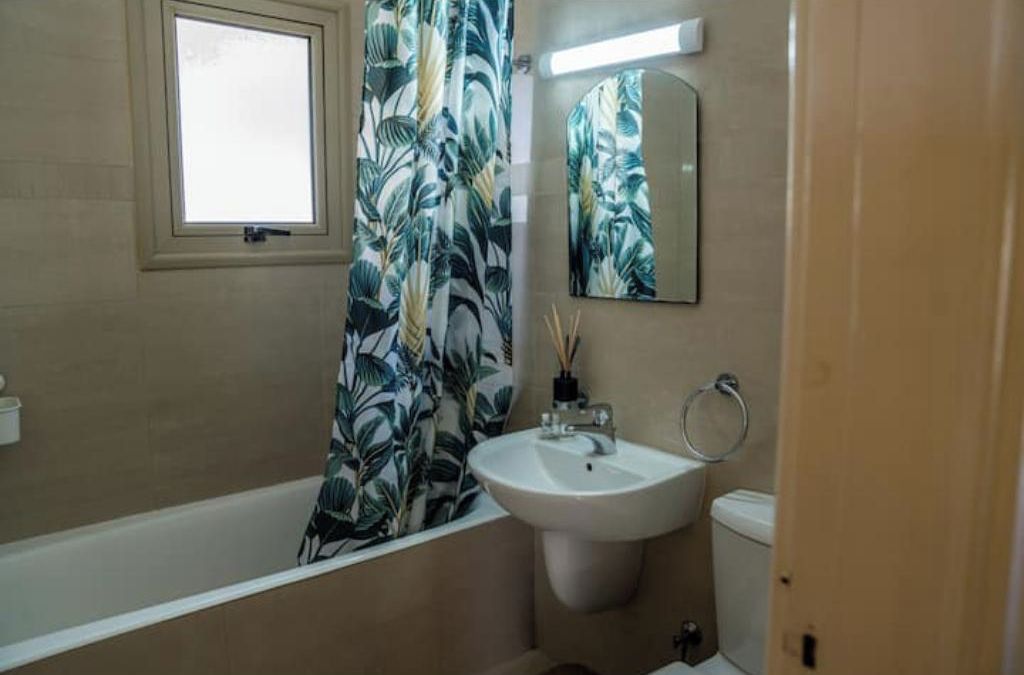 A bathroom with a bathtub, a sink, a toilet, a window, and a mirror.