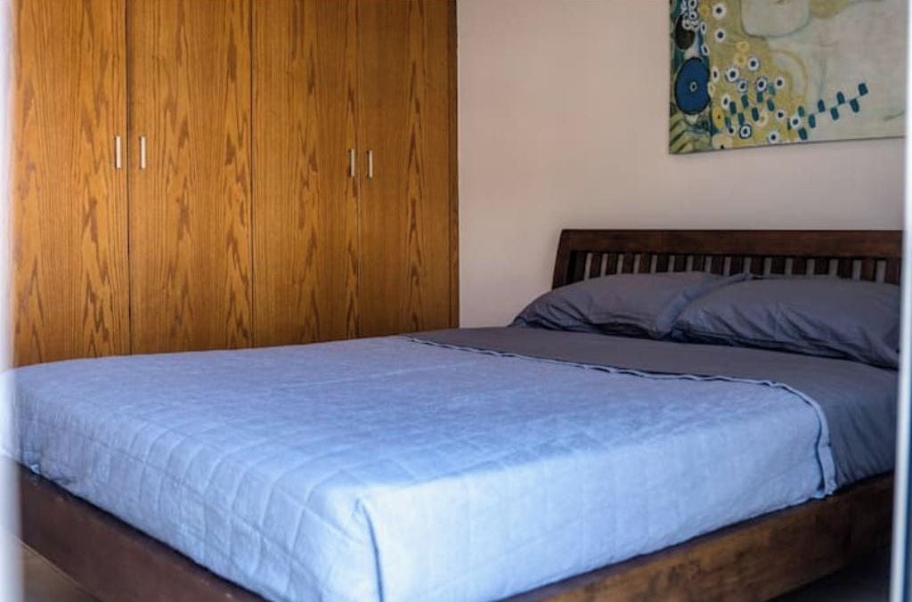 Un dormitorio con un armario de madera, una cama con colcha azul y un cuadro en la pared.