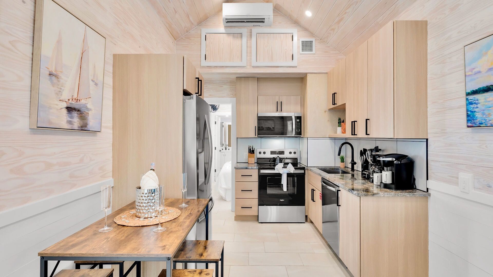 A compact kitchen with modern appliances, a dining area with a wooden table, and artwork on the walls.