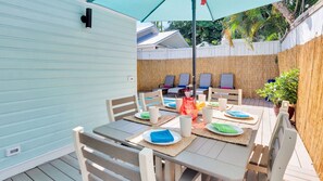An outdoor patio with a table set for dining, surrounded by chairs and a covered area with lounge chairs. - **SECRET SAND DOLLAR** Home & Pool + Last Key White Glove Service... (Key West)