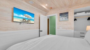 A bedroom with a bed, a painting of a beach scene, a closet with hanging clothes, and a green door. - **SECRET SAND DOLLAR** Home & Pool + Last Key White Glove Service... (Key West)