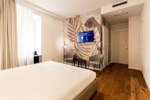 A hotel room with a bed, two chairs, a TV on the wall, and a wooden floor. - KT exclusive hotel (CAGLIARI)