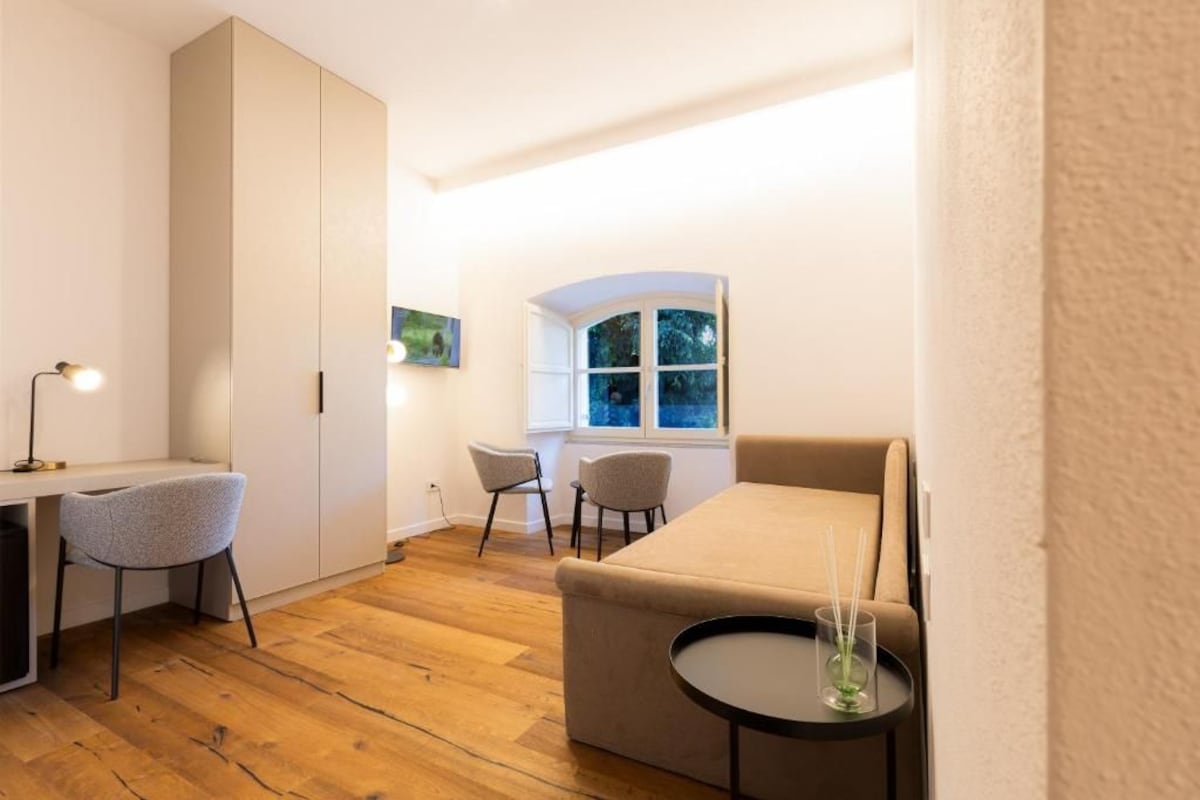 A compact room with a bed, a desk, two chairs, and a small table with a candle.