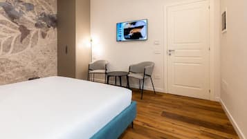 Quarto de hotel com cama, duas cadeiras, televisão e porta.