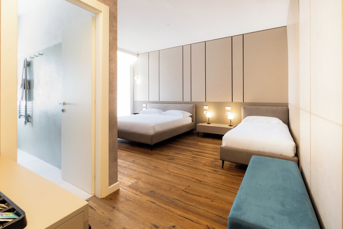 Habitación de hotel con dos camas, piso de madera y zona de ducha.