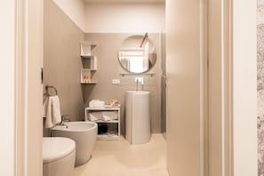 A modern bathroom with a toilet, bidet, and sink, and a glass shower enclosure. - KT exclusive hotel (CAGLIARI)