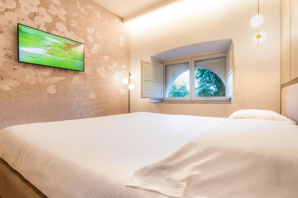 A bedroom with a bed, a television mounted on the wall, a window with a view of trees, and a light fixture.