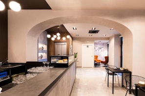 A modern kitchen with a central island, a dining area with chairs, and a hallway leading to a door. - KT exclusive hotel (CAGLIARI)