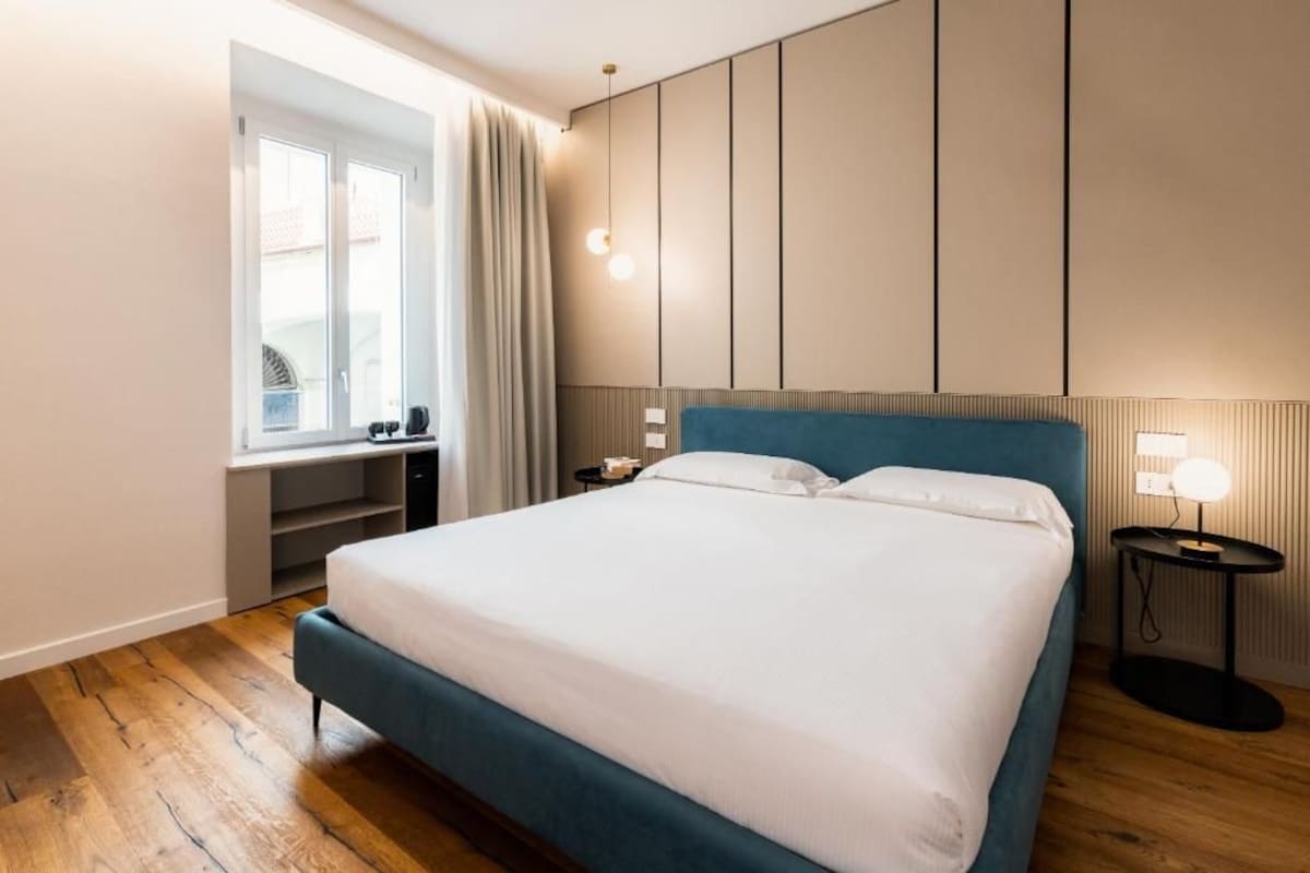 A modern bedroom with a large bed, a bedside table, a lamp, and a window with curtains.
