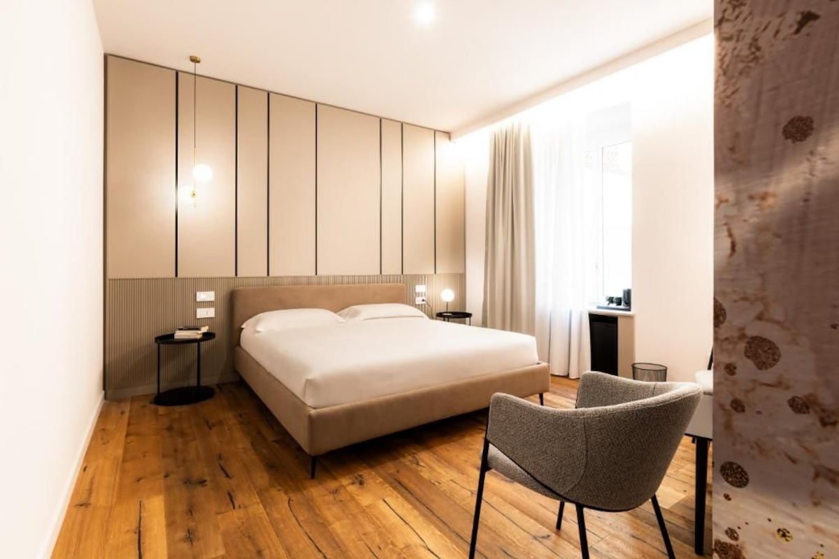 A hotel room with a bed, bedside tables, a chair, and a desk with a lamp.