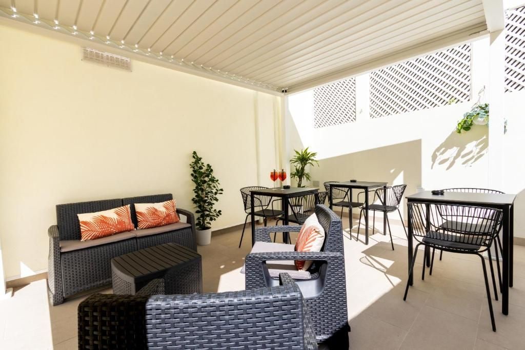 An outdoor seating area with a sofa, chairs, and tables, featuring a potted plant and a decorative wall.
