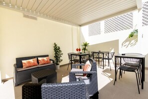An outdoor seating area with a sofa, chairs, and tables, featuring a potted plant and a decorative wall. - KT exclusive hotel (Cagliari)