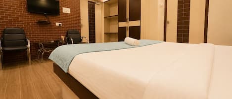 A hotel room with a bed, a desk, a chair, and a television mounted on a brick wall.