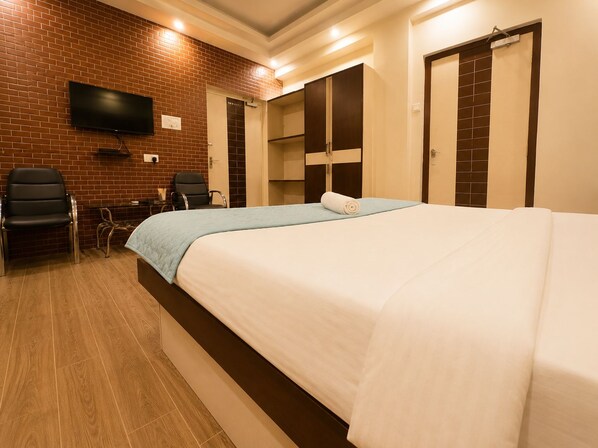 A hotel room with a bed, a desk, a chair, and a television mounted on a brick wall.