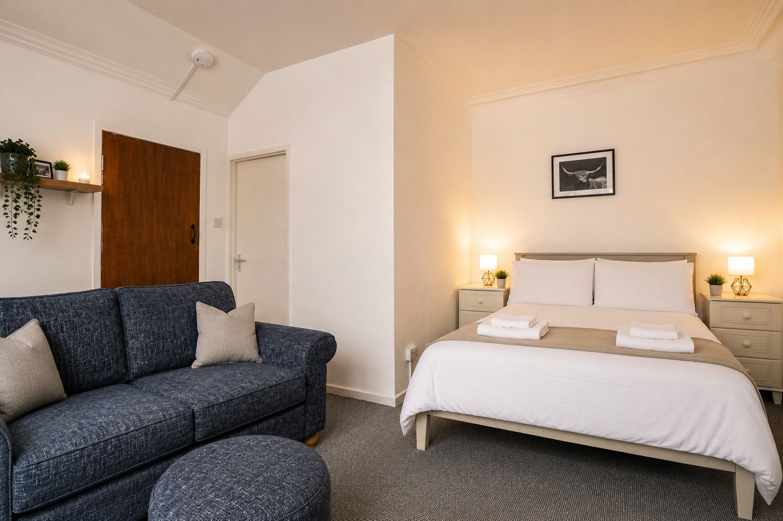 Een hotelkamer met een bed, een sofa, een nachtkastje met een lamp en een aan de muur hangend schilderij.