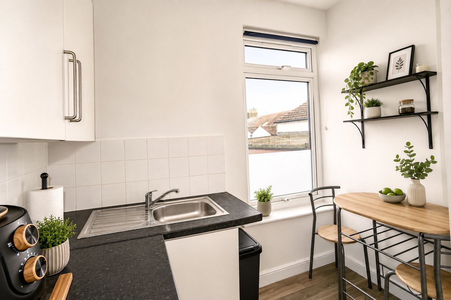 Een kleine keuken met een spoelbak, een raam en een eethoek met stoelen en een tafel.