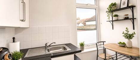A compact kitchen with a sink, a window, and a dining area with chairs and a table.
