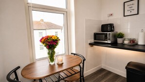 Eine kleine Küche mit Fenster, einer Mikrowelle, einem Toaster, einer Vase mit Blumen und einer Kerze auf einem Tisch.