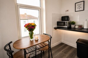 Una pequeña cocina con ventana, microondas, tostadora, un florero con flores y una vela sobre una mesa.