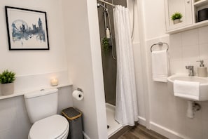 Baño con inodoro, ducha, lavamanos y un cuadro en la pared.