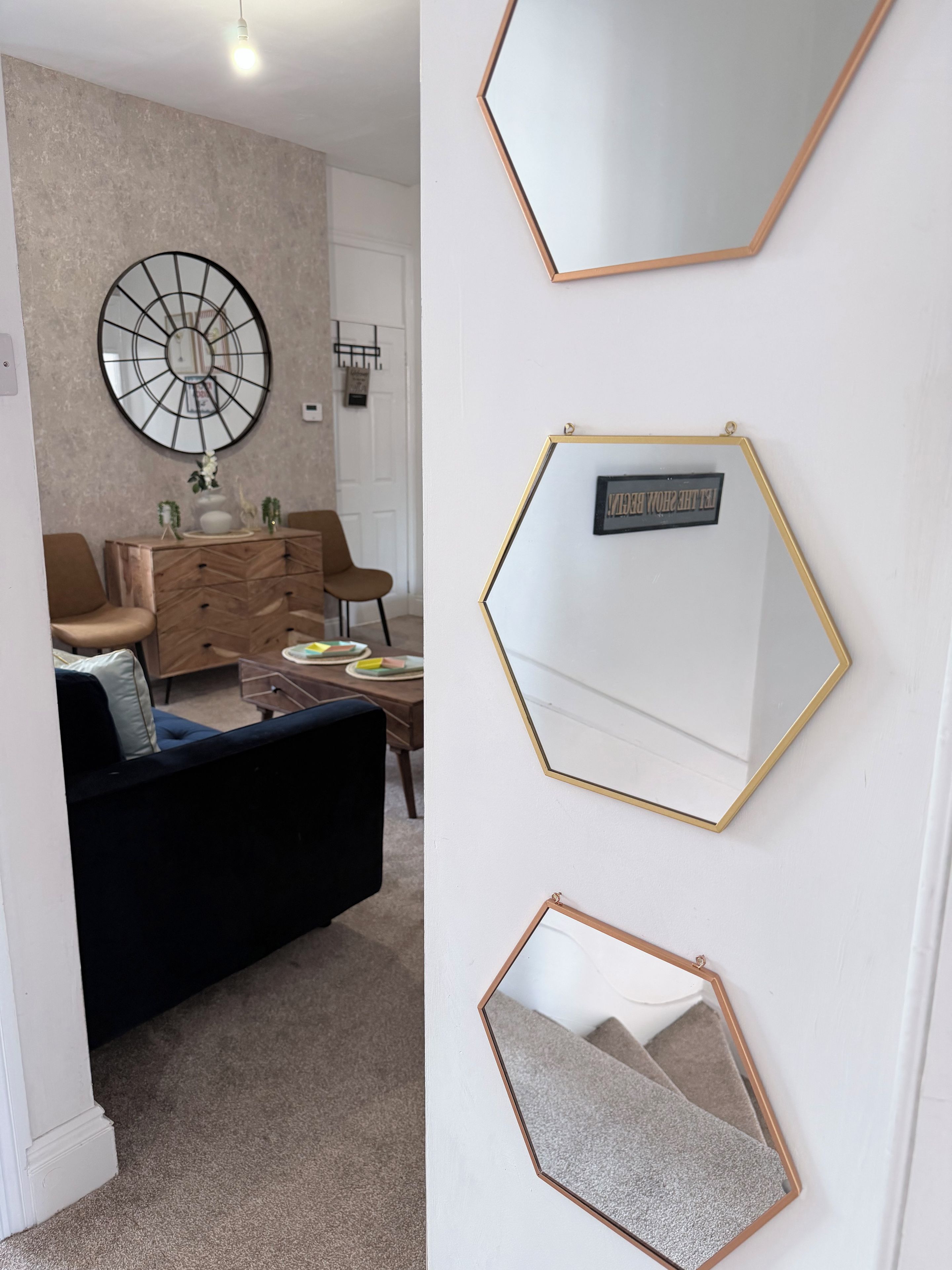Un salon agrémenté d’un miroir rond, d’un miroir hexagonal et d’une citation encadrée accrochée au mur.