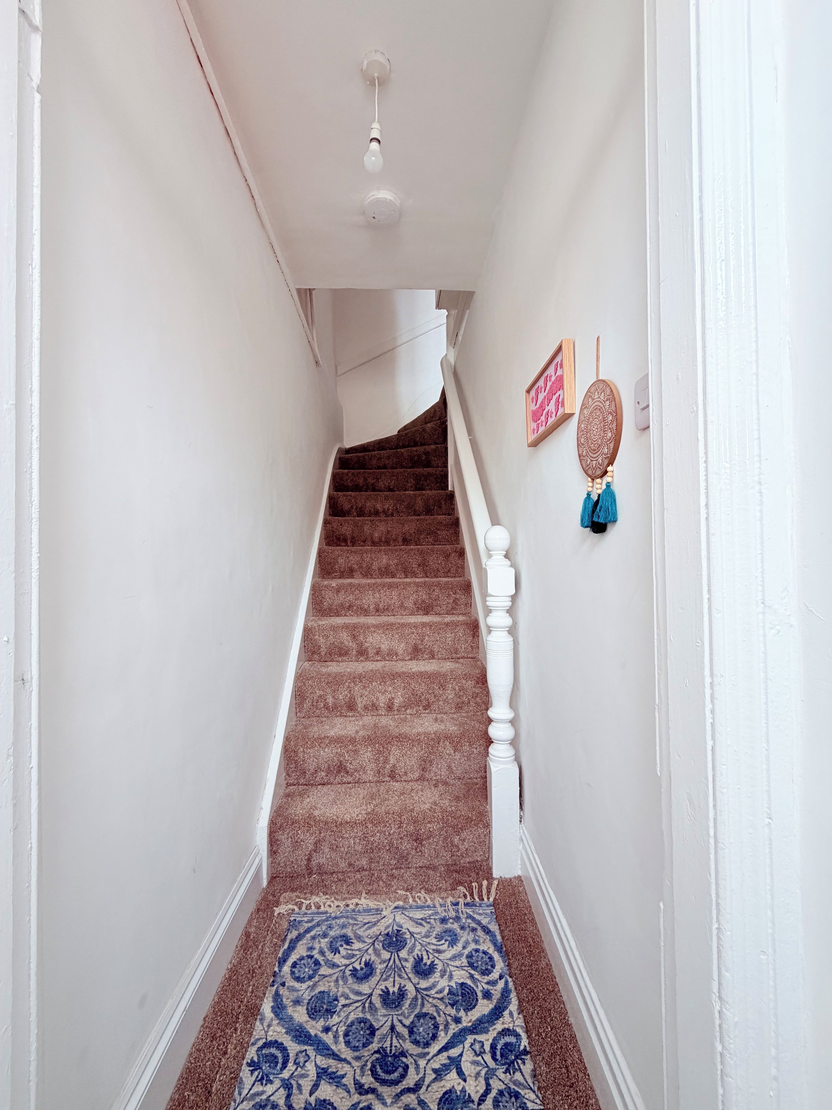A staircase with a patterned carpet leading to a landing with a ceiling light fixture.
