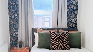 A bedroom with a bed, pillows, a nightstand, a window with curtains, and a view of the outside.