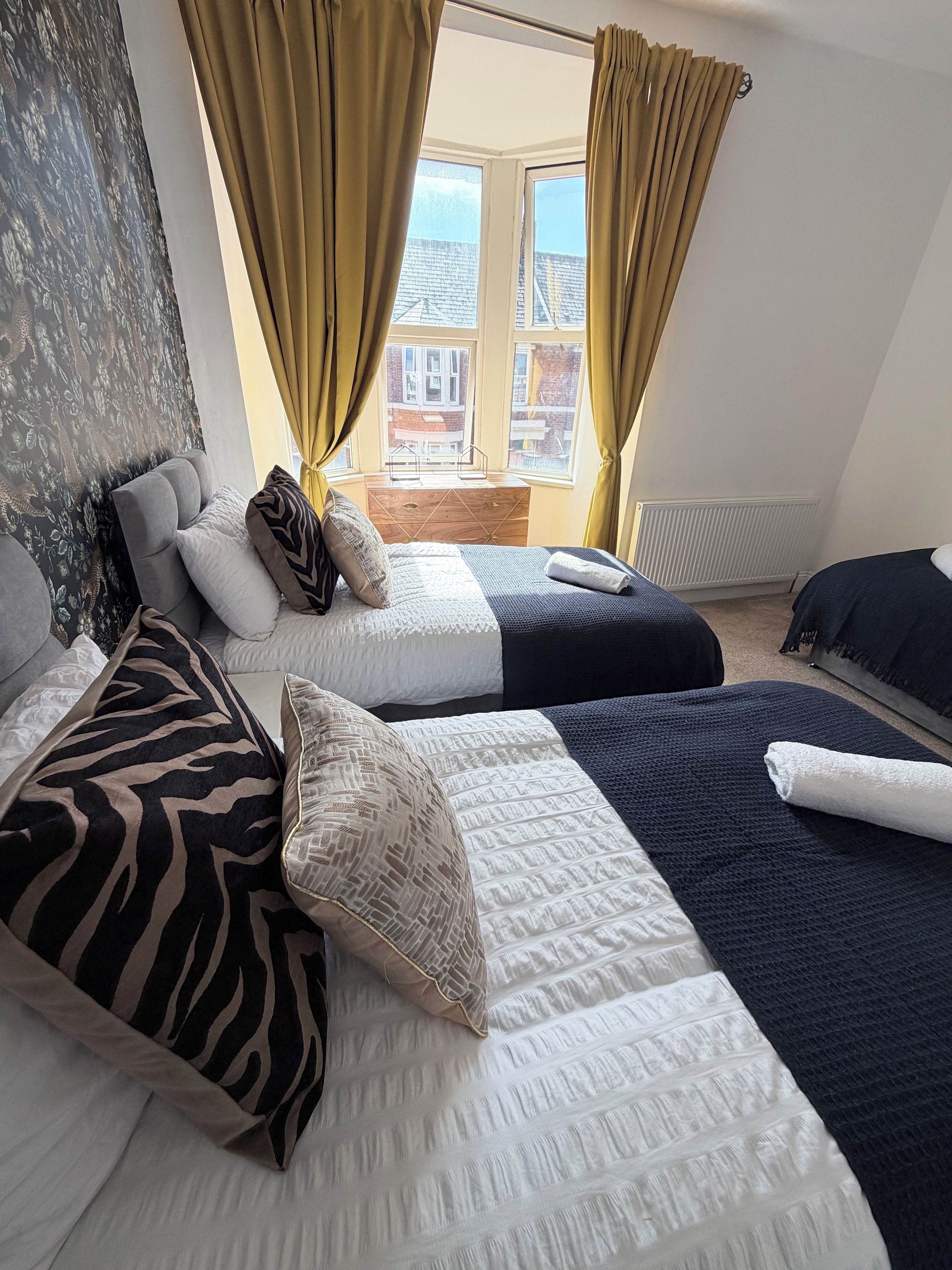 A bedroom with two beds, a window with curtains, and a view of buildings outside.